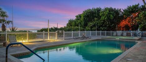 A rectangular swimming pool with a white fence and lounge chairs.