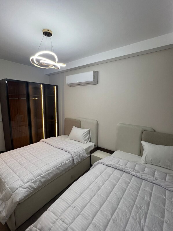 A bedroom with two beds, a wardrobe, an air conditioning unit, and a modern ceiling light fixture. - Spacious 3-bedroom apartment in charming Giza Governorate with AC (Giza Governorate)