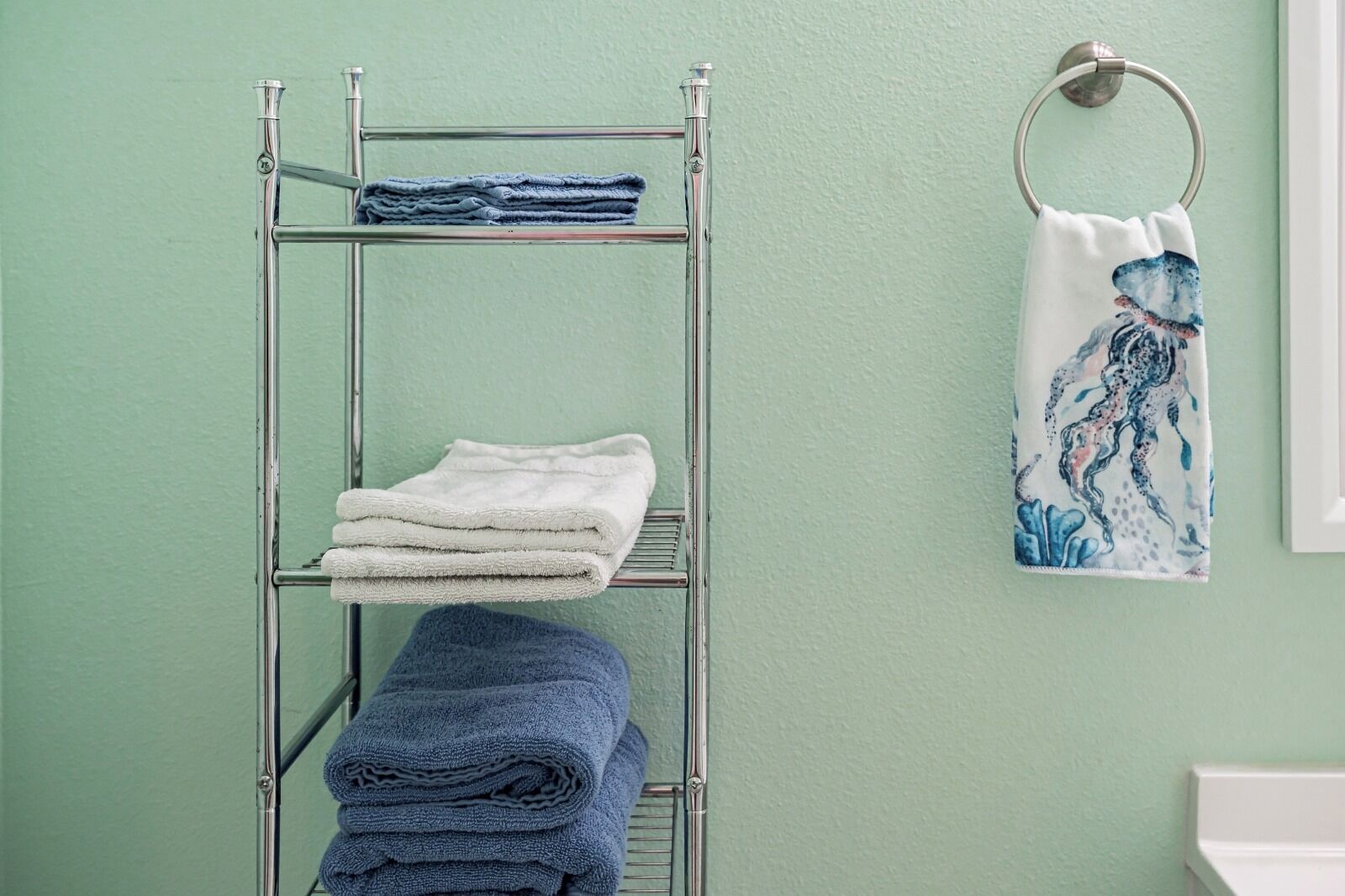 A metal drying rack with folded towels and a decorative towel hanging on the wall.