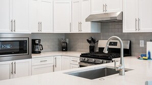 Uma cozinha moderna com armários brancos, eletrodomésticos de aço inoxidável e uma parede de azulejos cinza.