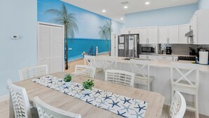 Uma cozinha moderna com armários brancos, micro-ondas embutido e vista para a praia através de um mural.