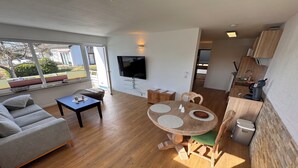 En moderne stue med sofa, sofabord, spisebord med stole, et fjernsyn ophængt på væggen og udsigt til det fri.