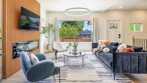 A modern living room with a flat-screen TV, a round coffee table, a sofa, and a chair. - AC / New Remodel / Chef's Kitchen / BBQ / Cap Hill (Seattle)