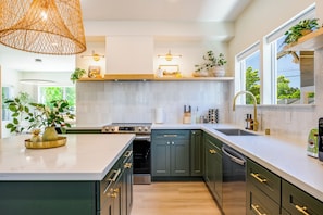 A modern kitchen with a large island, built-in appliances, and a window overlooking greenery. - AC / New Remodel / Chef's Kitchen / BBQ / Cap Hill (Seattle)