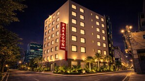 A multi-story hotel with a prominent 'PARAGON SUITES' sign, surrounded by palm trees and street lamps. - Hotel Paragon Suites (New Delhi)