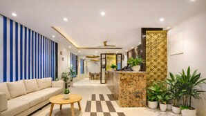 A modern hotel lobby with a sofa, coffee table, reception desk, and potted plants. - Hotel Paragon Suites (New Delhi)