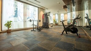A gym with exercise equipment, large windows, and a potted plant. - Hotel Paragon Suites (New Delhi)
