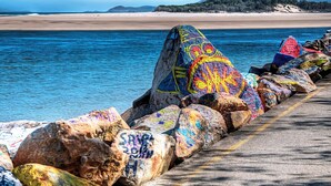 A pier with colorful graffiti on rocks and a beach in the background. - Coastal Calm - Stylish Escape in Heart of Nambucca (Nambucca Heads)