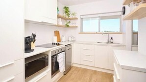 A modern kitchen with white cabinets, a built-in oven, a dishwasher, and a window above the sink. - Coastal Calm - Stylish Escape in Heart of Nambucca (Nambucca Heads)
