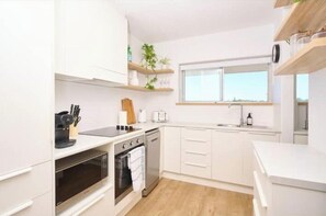 Una cocina moderna con armarios blancos, horno integrado, lavavajillas y una ventana sobre el fregadero.