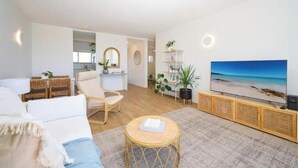 A modern living room with a sofa, a chair, a small round table, a television, and a bookshelf. - Coastal Calm - Stylish Escape in Heart of Nambucca (Nambucca Heads)