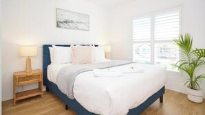 A bedroom with a bed, bedside lamps, a window, and a plant. - Coastal Calm - Stylish Escape in Heart of Nambucca (Nambucca Heads)