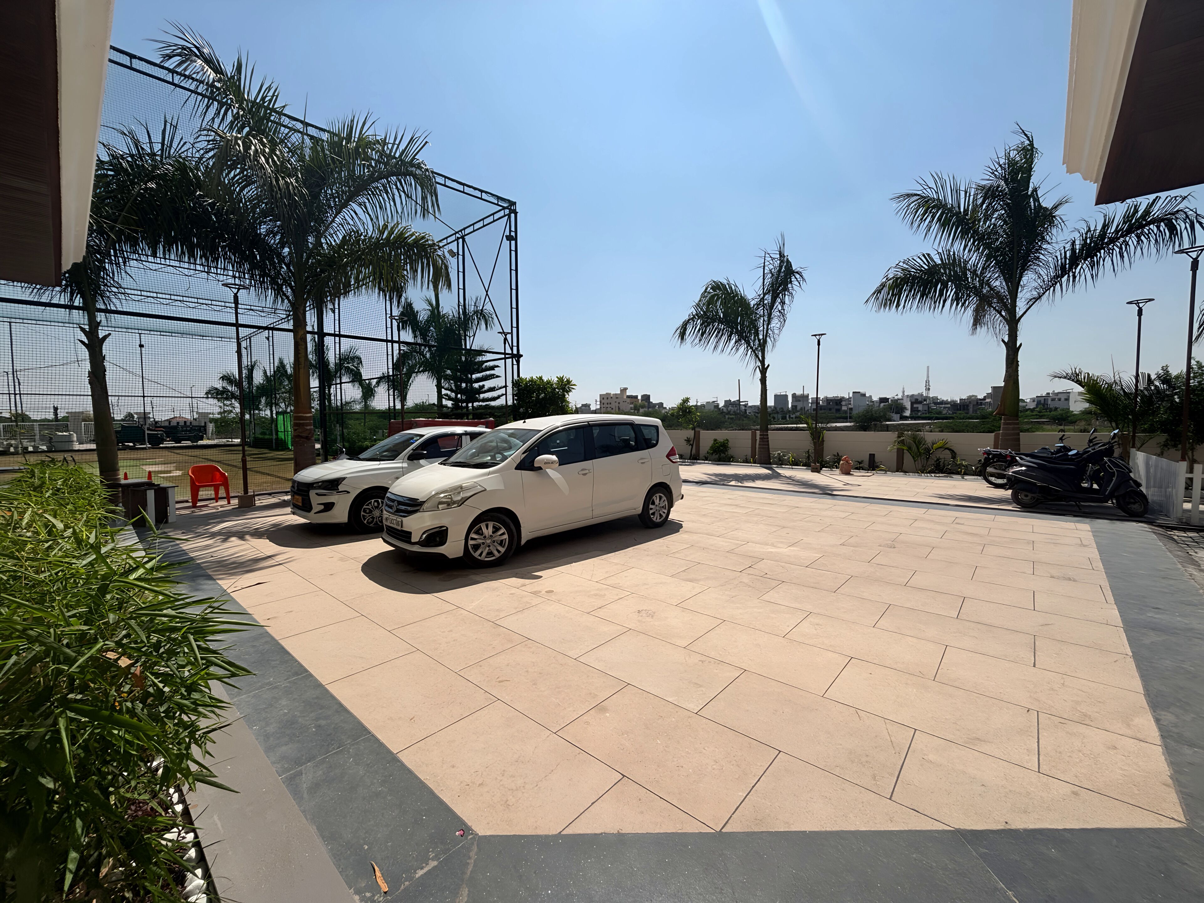 A parking area with two white cars, palm trees, and a clear sky.