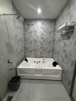 A modern bathroom with a freestanding bathtub, a showerhead, a towel rack, and a trash bin.