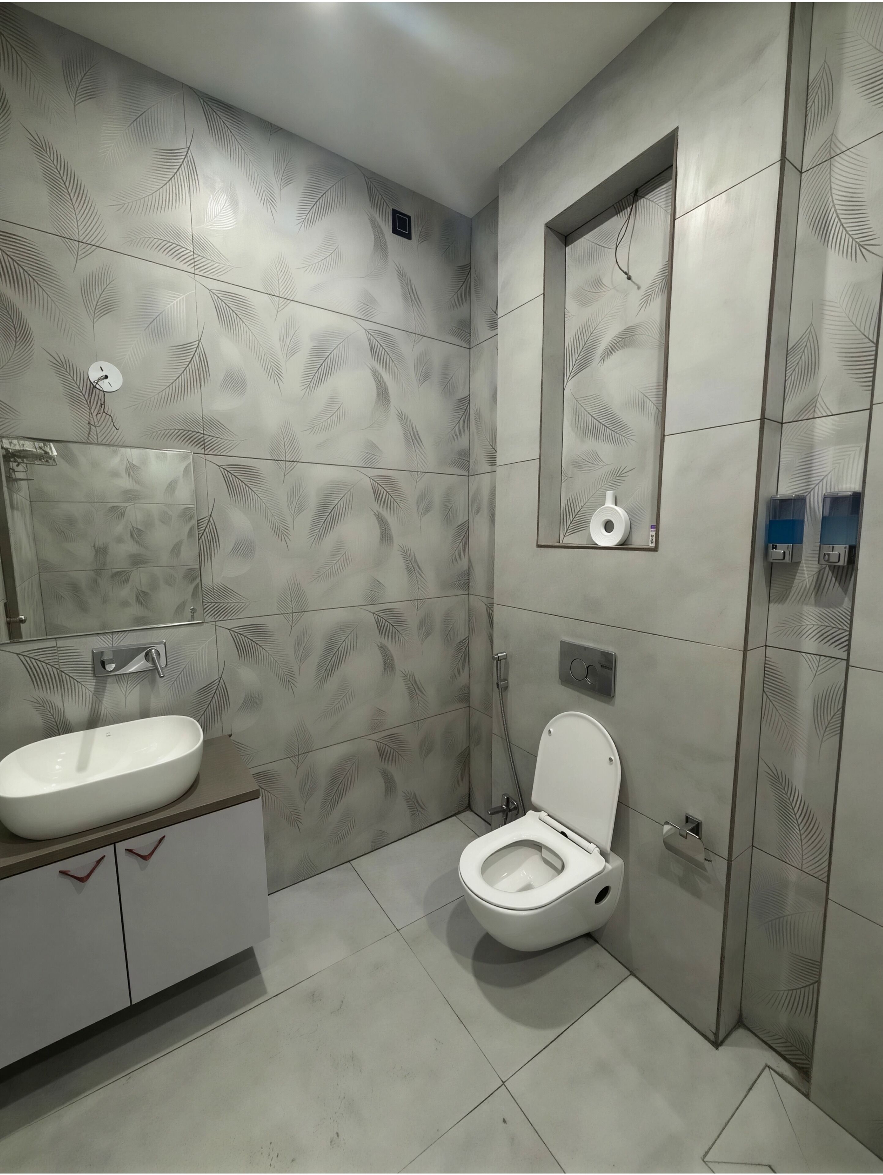 A bathroom with a sink, toilet, and a mirror with a leaf pattern.