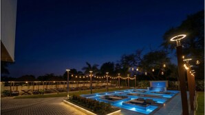 A pool area with multiple seating arrangements and a covered section, surrounded by trees and string lights. - Shree Agrawal Avenue (Ujjain)