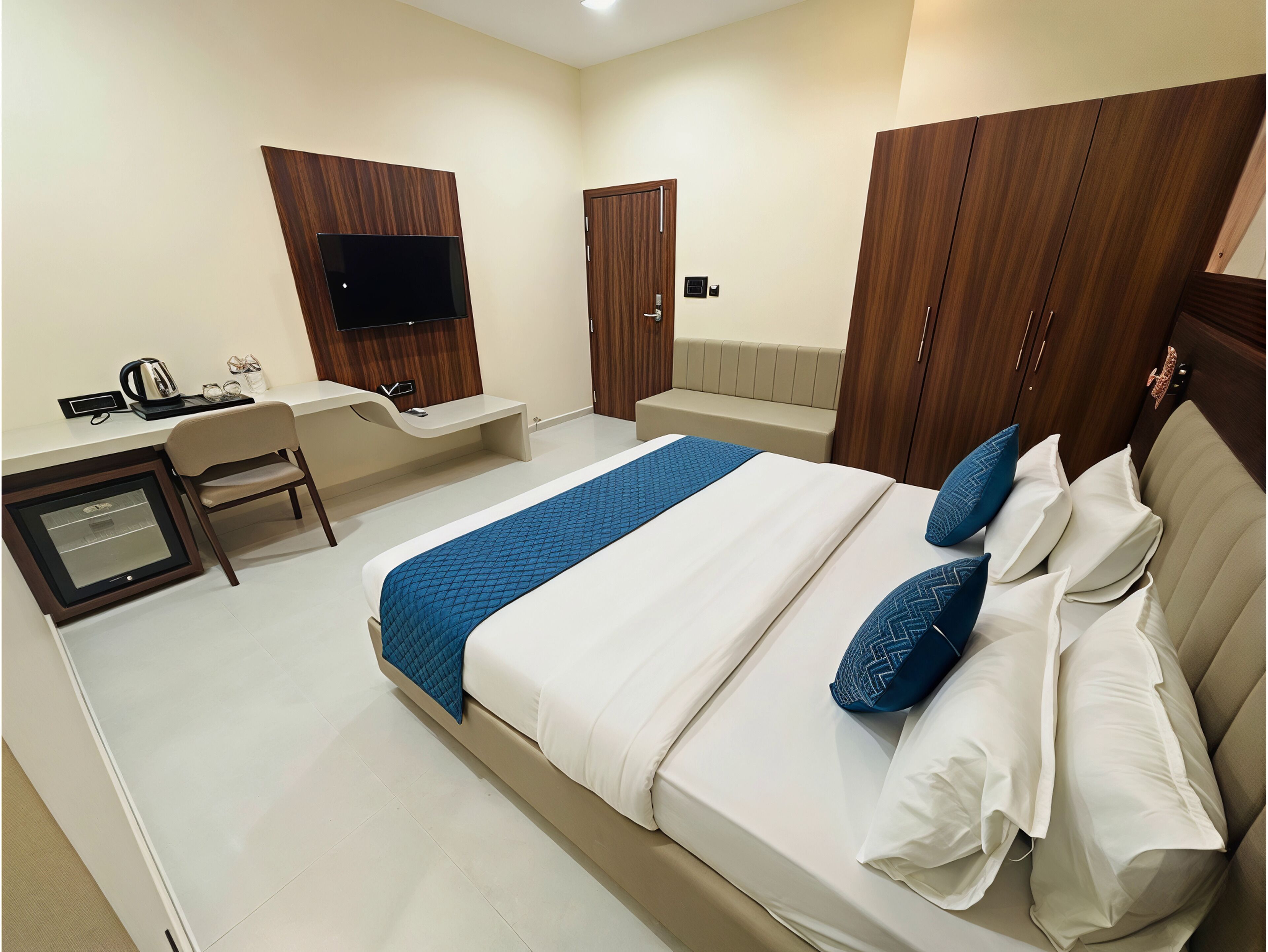 A hotel room with a bed, a desk with a TV, a chair, and a wardrobe.