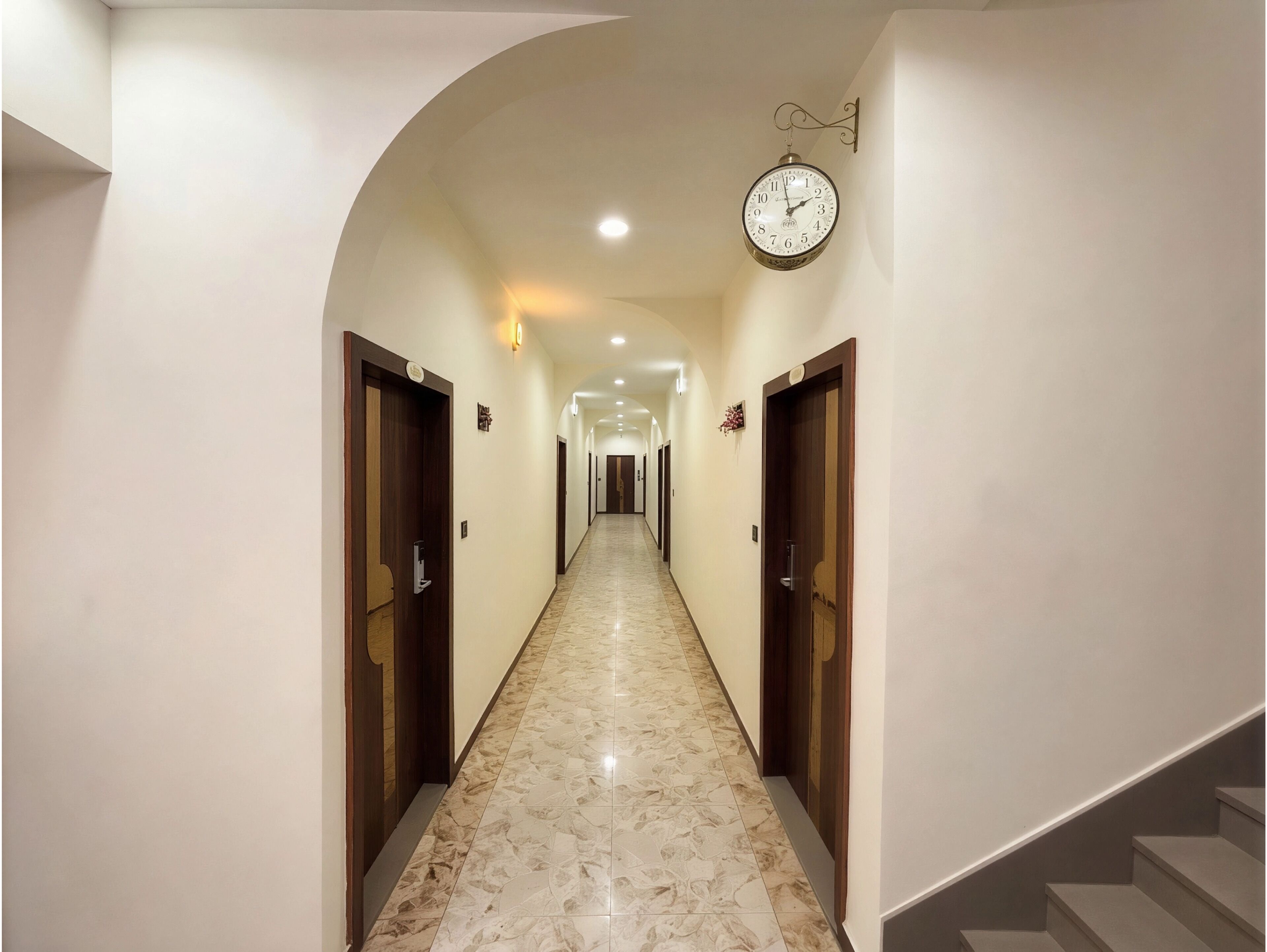 A hotel hallway with marble flooring, wooden doors, and a wall-mounted clock.