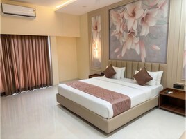 A hotel room with a large bed, a nightstand, a wall-mounted air conditioner, and a large floral painting.