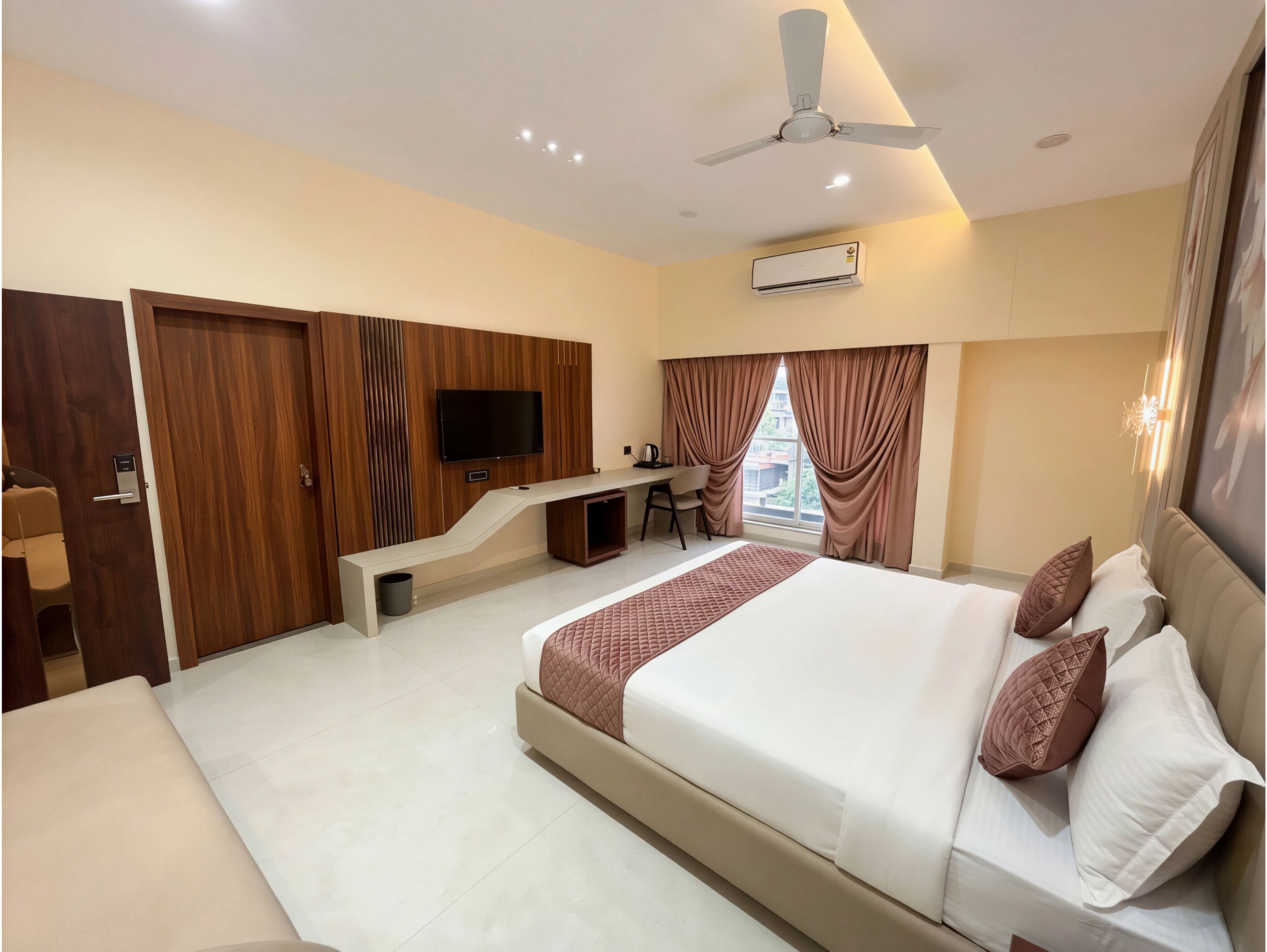 A hotel room with a bed, desk, TV, and an air conditioning unit.