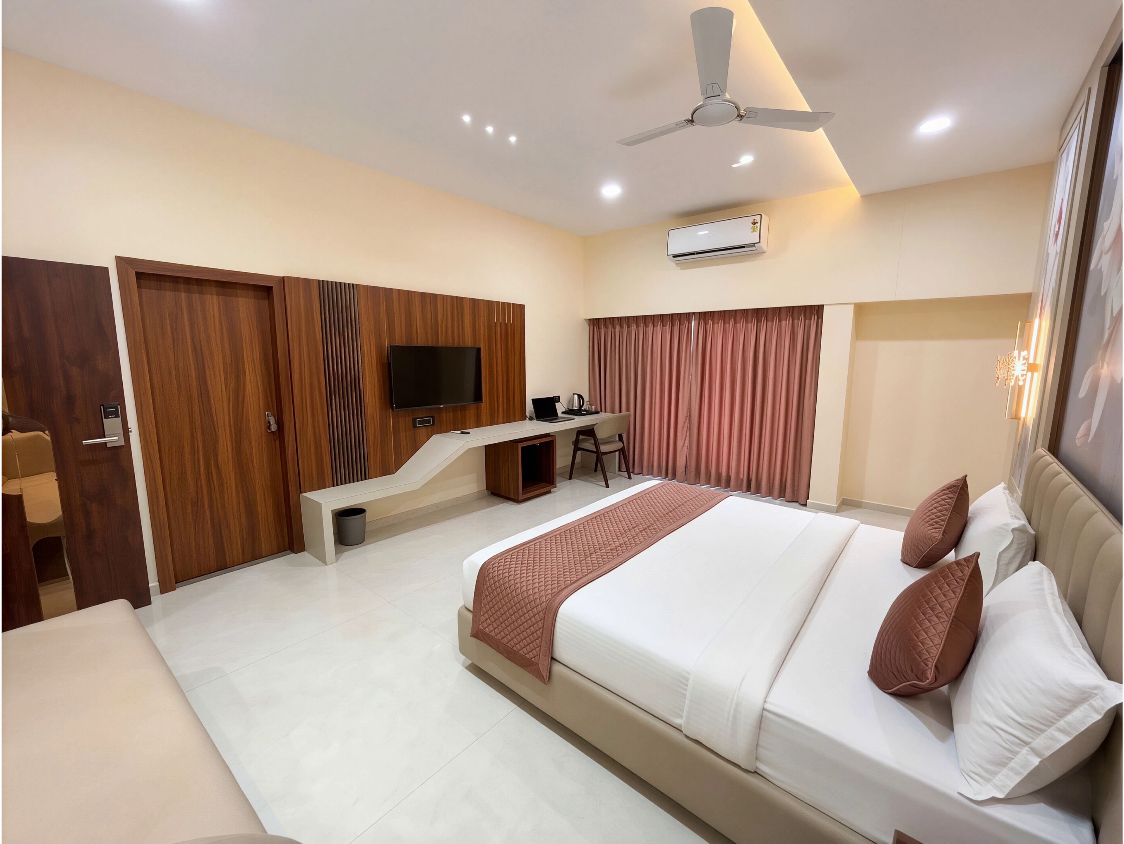 A hotel room with a bed, desk, chair, TV, ceiling fan, and air conditioning unit.