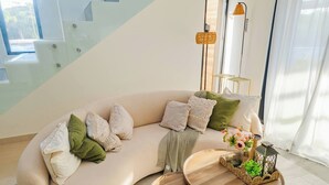 Una sala de estar moderna con un sofá curvo, una mesa de centro redonda de madera y una mesita auxiliar con un jarrón de flores.