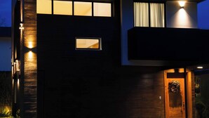 Una casa moderna de dos pisos con una entrada bien iluminada, un ventanal visible y un camino que lleva a la puerta.
