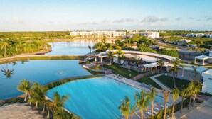 Un resort con una amplia piscina central, palmeras y vistas del paisaje circundante.