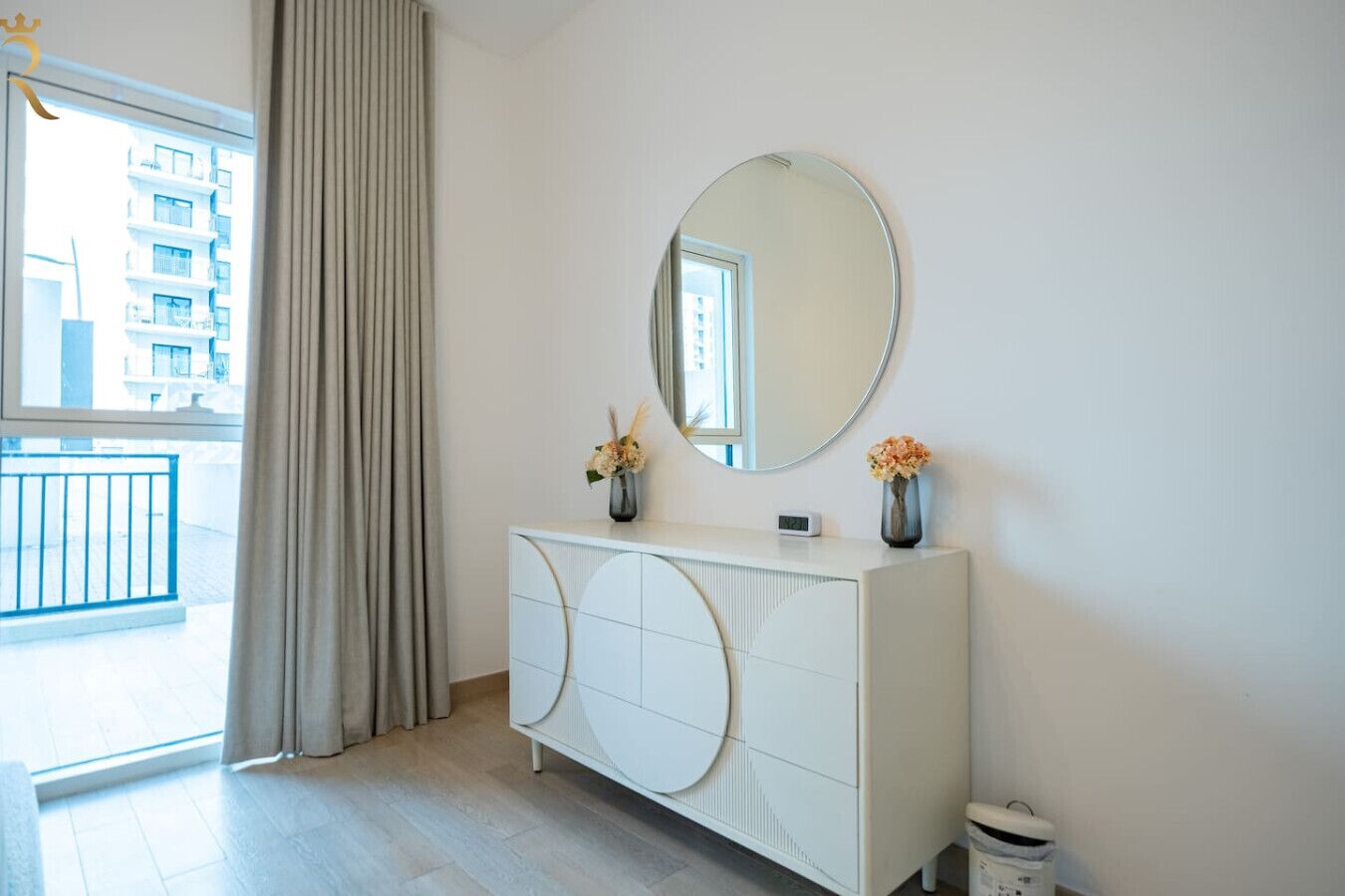 A modern room with a white console table, a round mirror, and two vases with flowers.