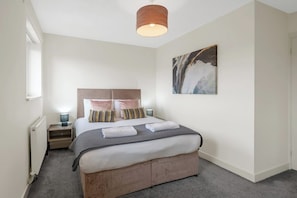 Een slaapkamer met een bed, nachtkastjes, een radiator, een aan de muur hangend kunstwerk en een plafondlamp.