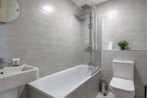 Een moderne badkamer met bad, toilet, wastafel en een kleine plant in pot.