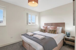 Een slaapkamer met een groot bed, een nachtkastje, een lamp en een raam.