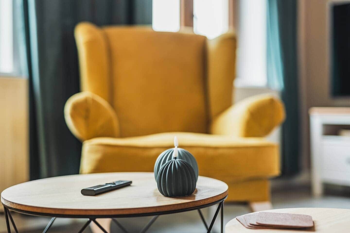 Una poltrona gialla, un tavolino rotondo in legno con un telecomando e un piccolo oggetto decorativo.