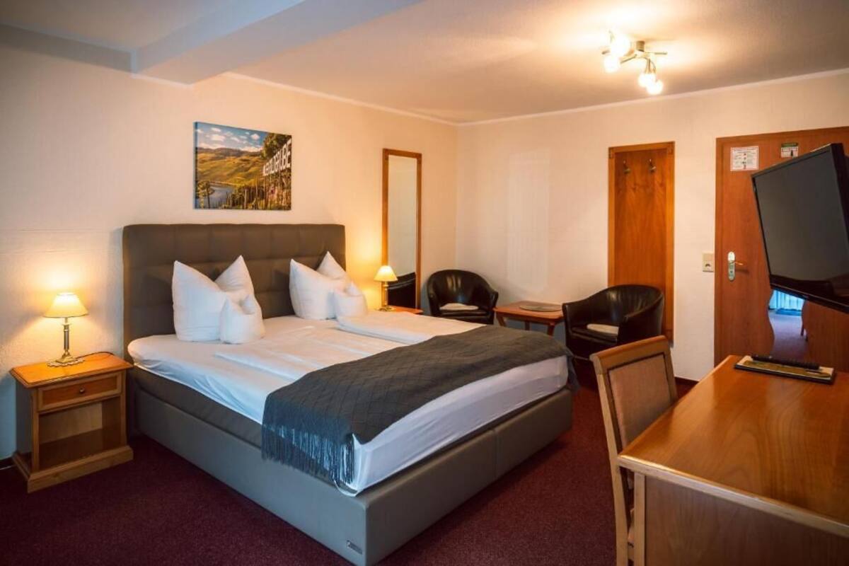 A hotel room with a bed, bedside tables, a desk, a chair, a television, and a mirror.