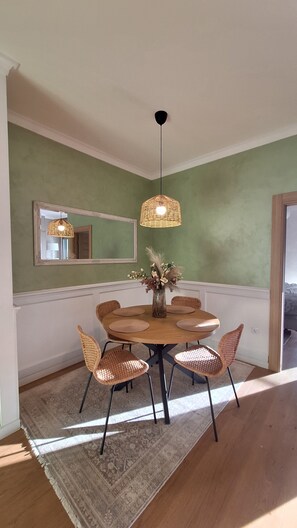 A dining area with a round table, wicker chairs, a vase with dried flowers, a hanging light fixture, and a mirror on the wall. - Olive Residence Mira (Petrovac)