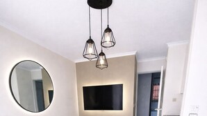 Una sala de estar moderna con un sofá gris, una mesa de centro, un televisor de pantalla plana montado en la pared y un espejo redondo.