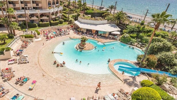 Un resort con piscina central, zona de playa y vistas al mar.