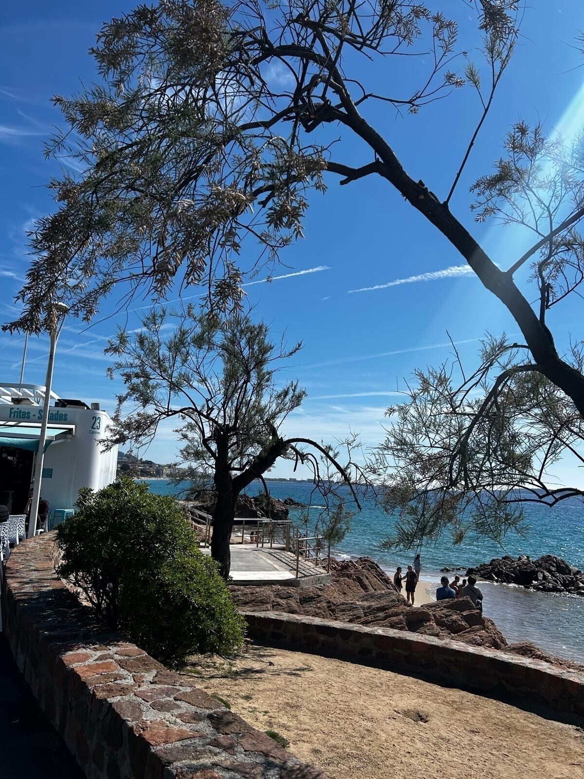 Une zone côtière avec un mur de pierre, un arbre et un bâtiment portant l’inscription « Frites - Slades ».