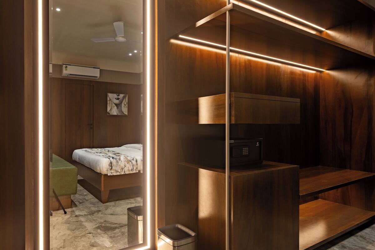 A modern bedroom with a large mirror, a bed, a built-in wardrobe, and a small kitchenette.