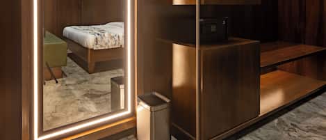 A modern bedroom with a large mirror, a bed, a built-in wardrobe, and a small kitchenette.