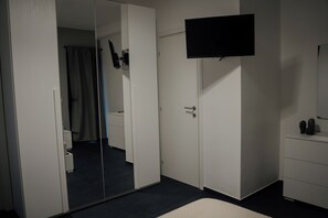 Een slaapkamer met een bed, een aan de muur bevestigde televisie, een kledingkast en een spiegel.