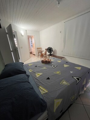 Ein Schlafzimmer mit einem Bett, einem Ventilator, einem Sessel und einem Tisch.