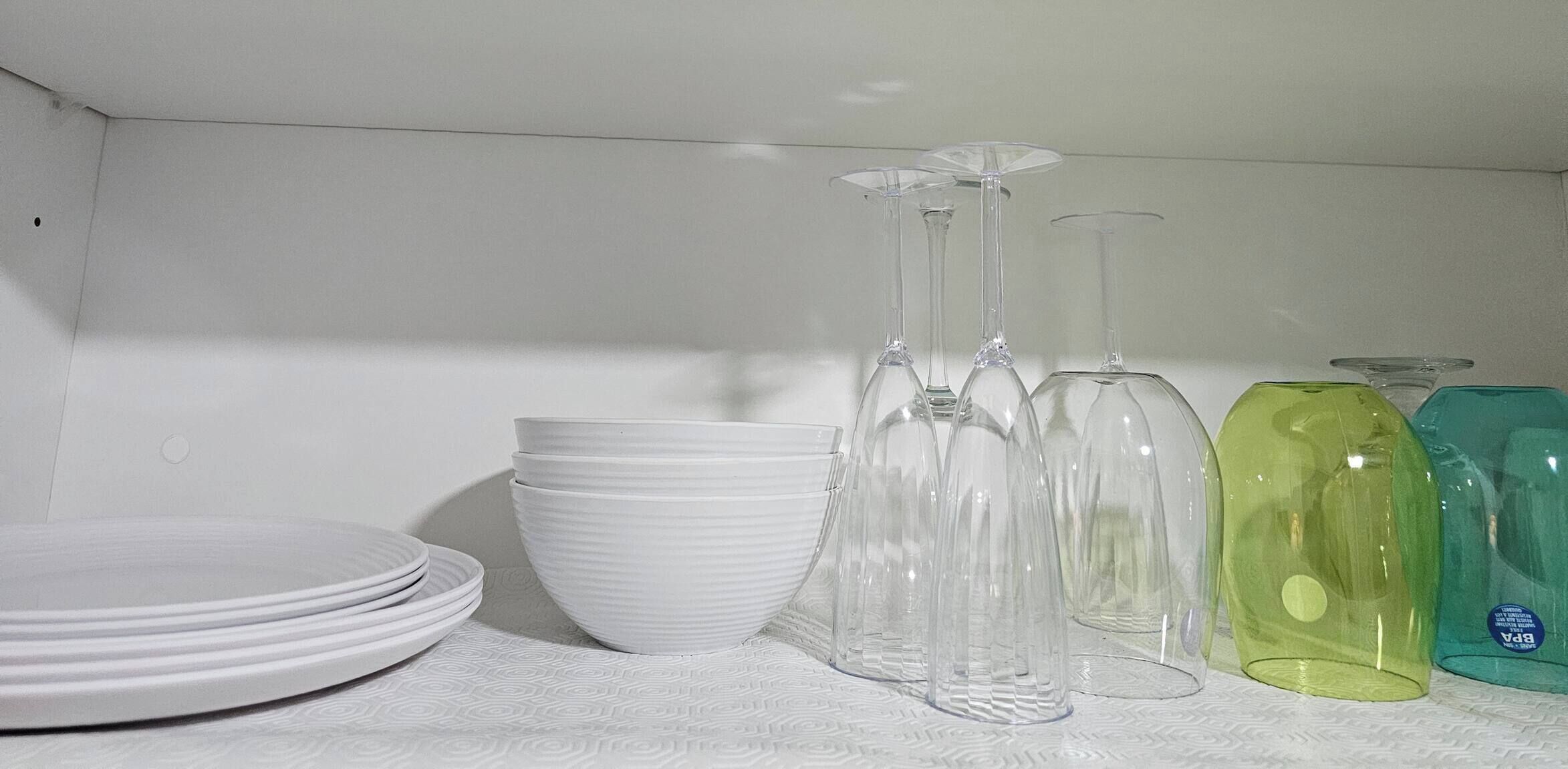 Ein Regal mit weißen Tellern, klaren Weinkästen und farbigen Glasflaschen.