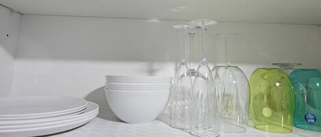 Ein Regal mit weißen Tellern, klaren Weinkästen und farbigen Glasflaschen.