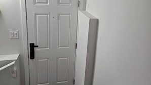 Une porte blanche avec une poignée noire, un mur blanc et un paillasson noir.