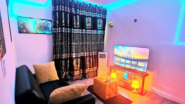 Un salon avec un canapé noir, un téléviseur, une petite table et un rideau à motifs.