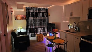 Une cuisine compacte avec un coin repas, un rideau noir à motifs, une petite table avec des chaises et un canapé.