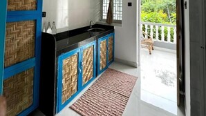A modern kitchen with a black countertop, blue cabinets with a woven pattern, a window with a view of greenery, and a balcony with a railing. - Salt & Coco (Ashvem)