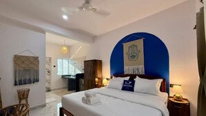 A hotel room with a bed, a desk, a chair, a hanging tapestry, and a wall-mounted artwork. - Salt & Coco (Ashvem)