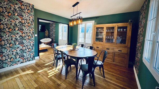 Een eetruimte met een houten tafel en stoelen, een kast met glazen, en een wand met een patroon.